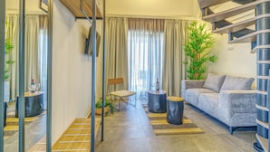 A modern living room with a grey sofa, a wooden coffee table, a round side table, a wicker chair, and a spiral staircase. - Miroes Suites (Sithonia)