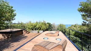 A wooden deck with built-in seating and a stone wall, overlooking a coastal area with trees and a clear sky. - Spacious house with pool and beach access (Les Portes-en-Ré)