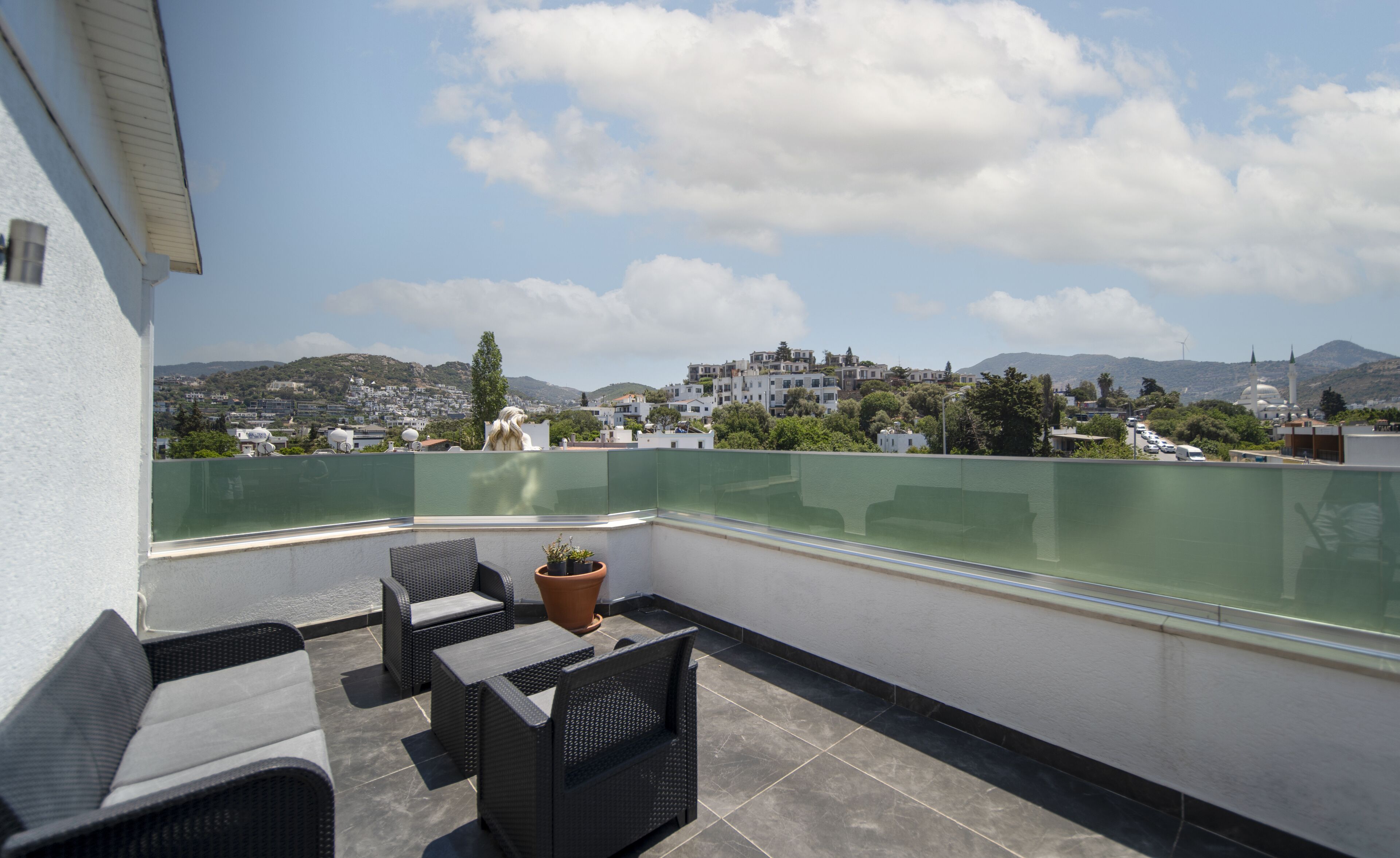 A rooftop terrace with outdoor furniture, a view of a cityscape, and a mountain in the background.