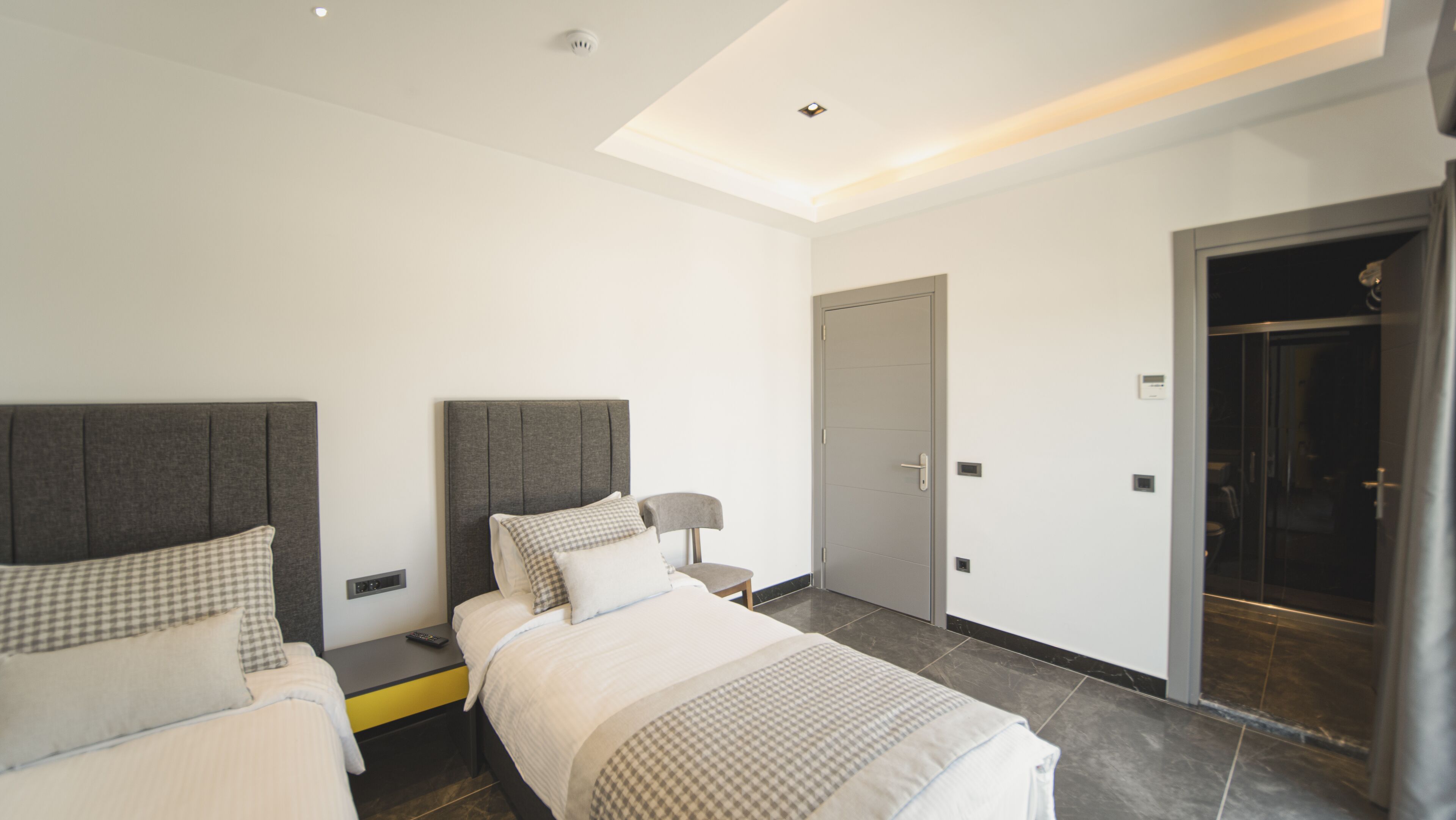 Een moderne hotelkamer met twee bedden, een nachtkastje, een lamp en een deur naar een badkamer.
