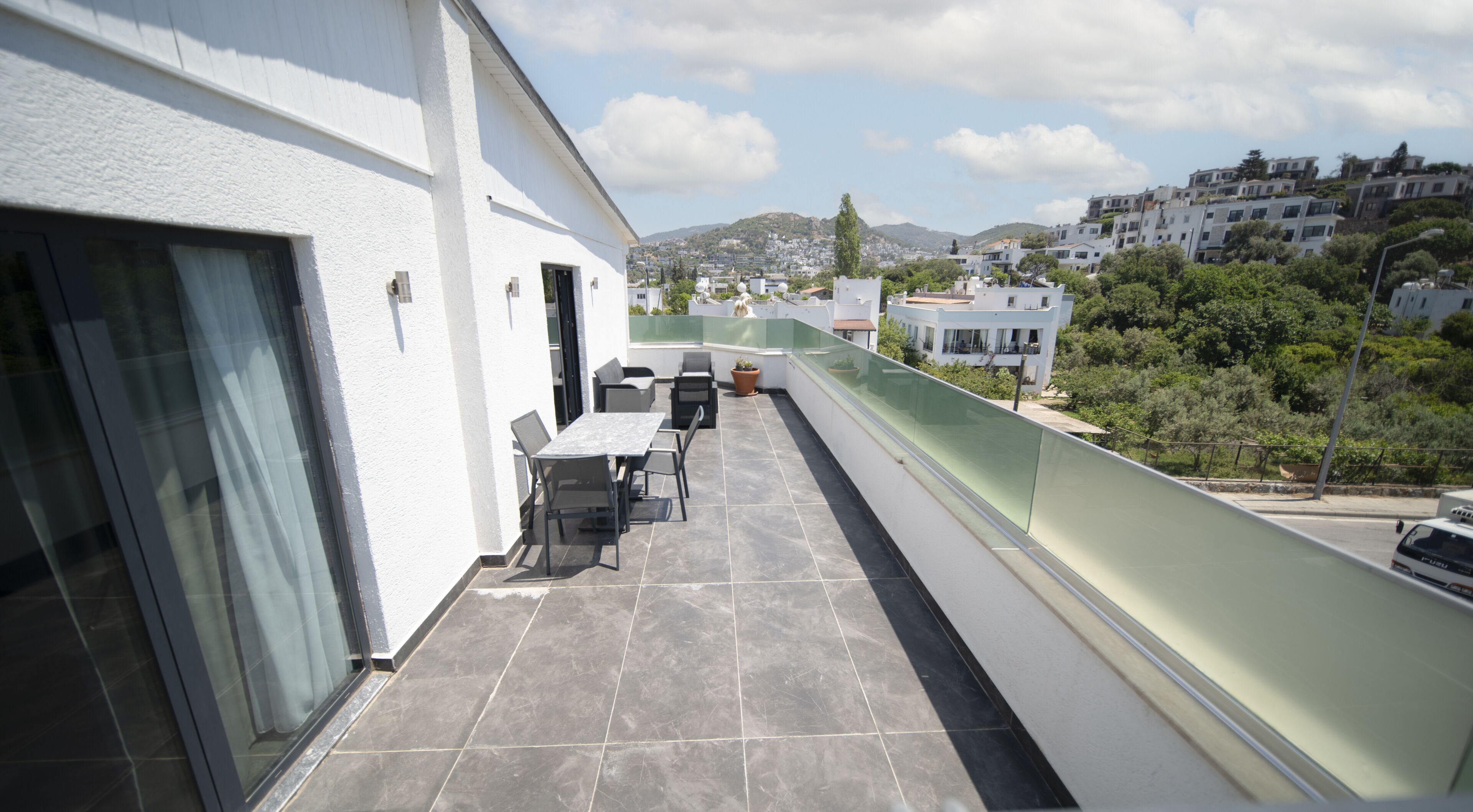 Ein Balkon mit Tisch und Stühlen, eine Glastür und Blick auf eine Hügelkuppe mit Gebäuden.