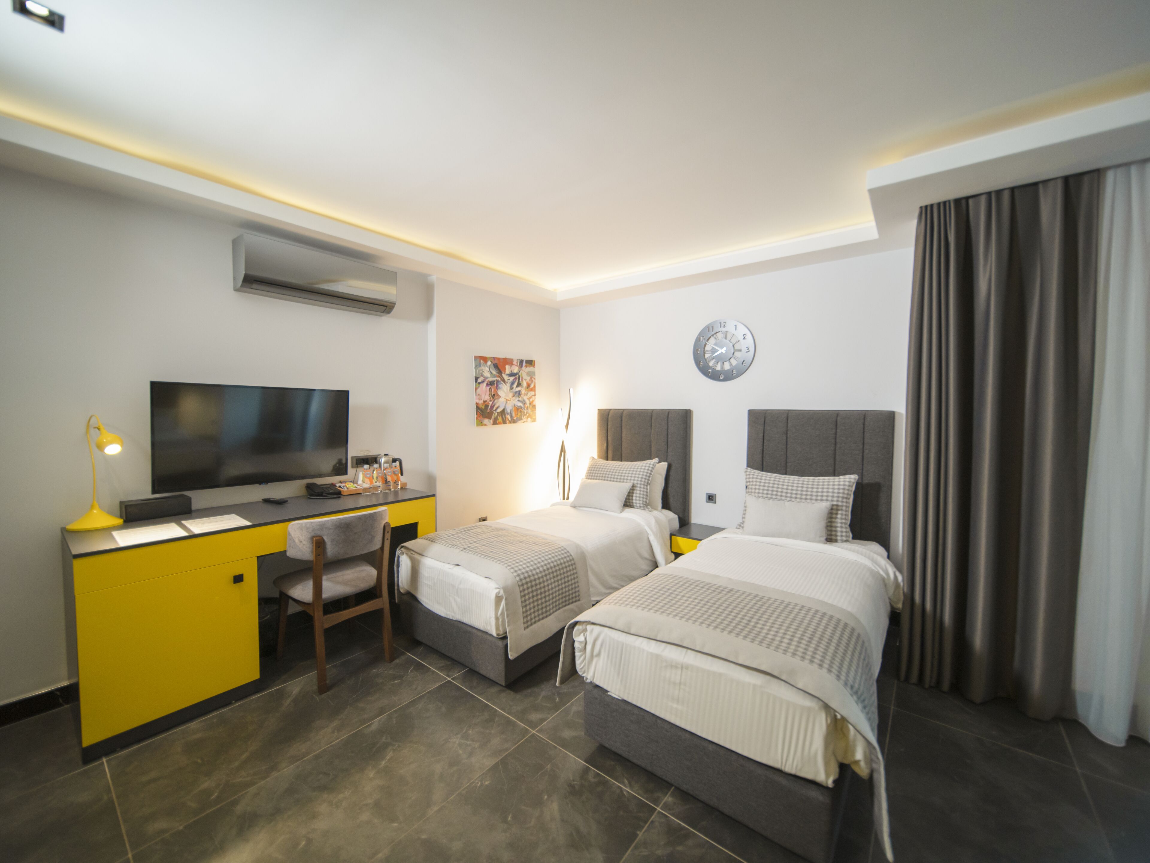 A hotel room with a desk, two beds, a TV, and a clock on the wall.