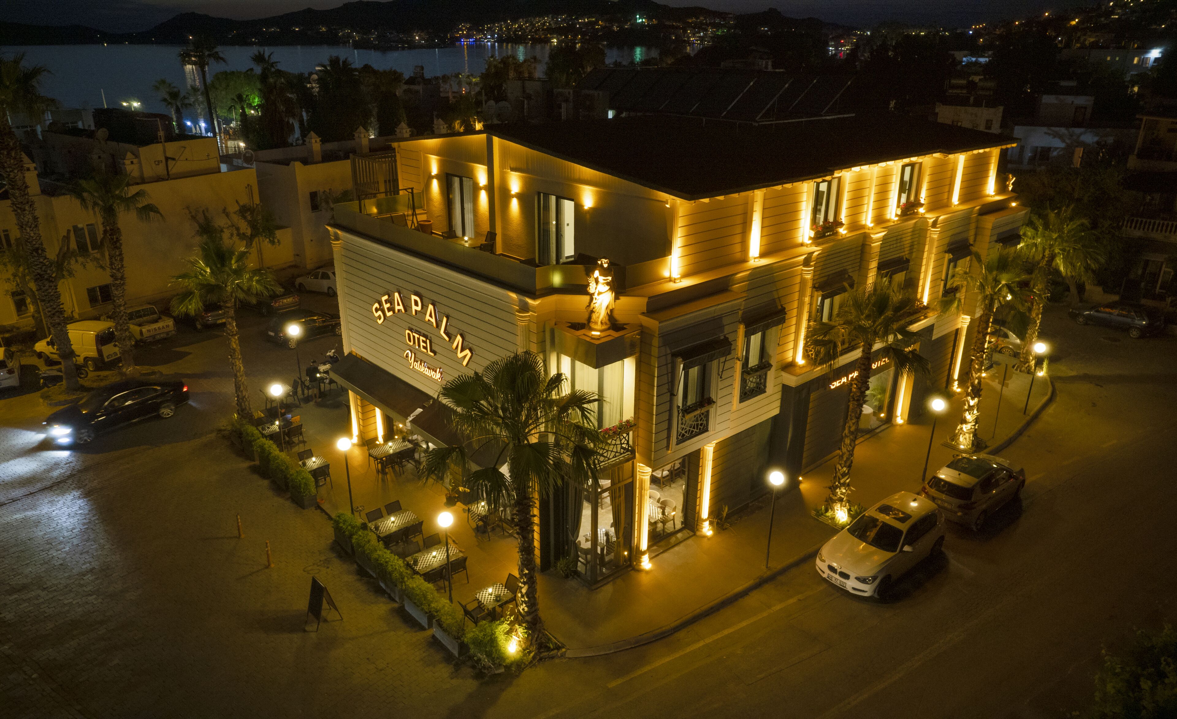 Un hotel con un letrero llamativo, asientos al aire libre y vistas de la ciudad de noche.