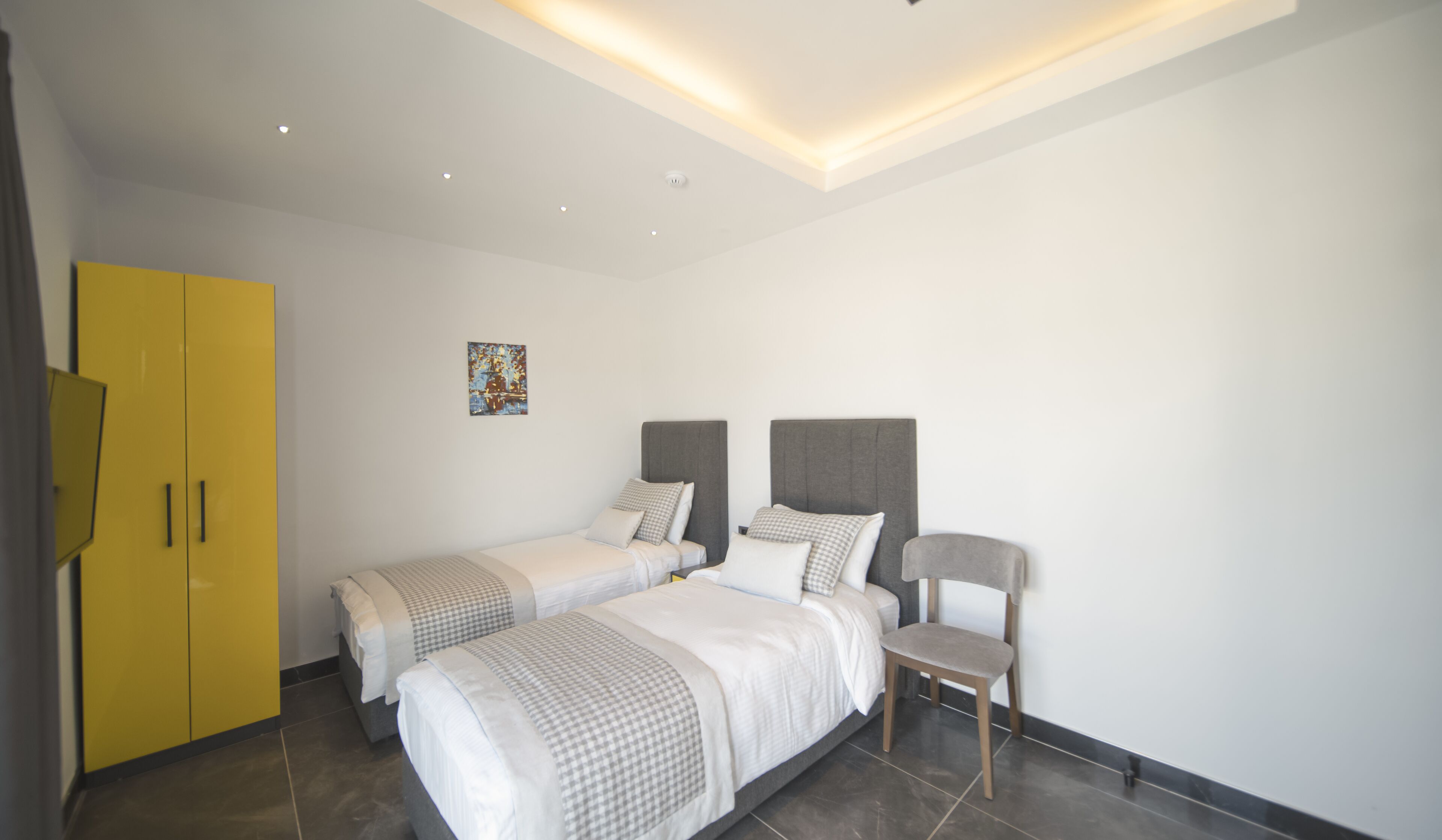 A modern hotel room with two single beds, a chair, and a yellow wardrobe.