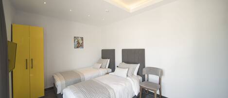 A modern hotel room with two single beds, a chair, and a yellow wardrobe.