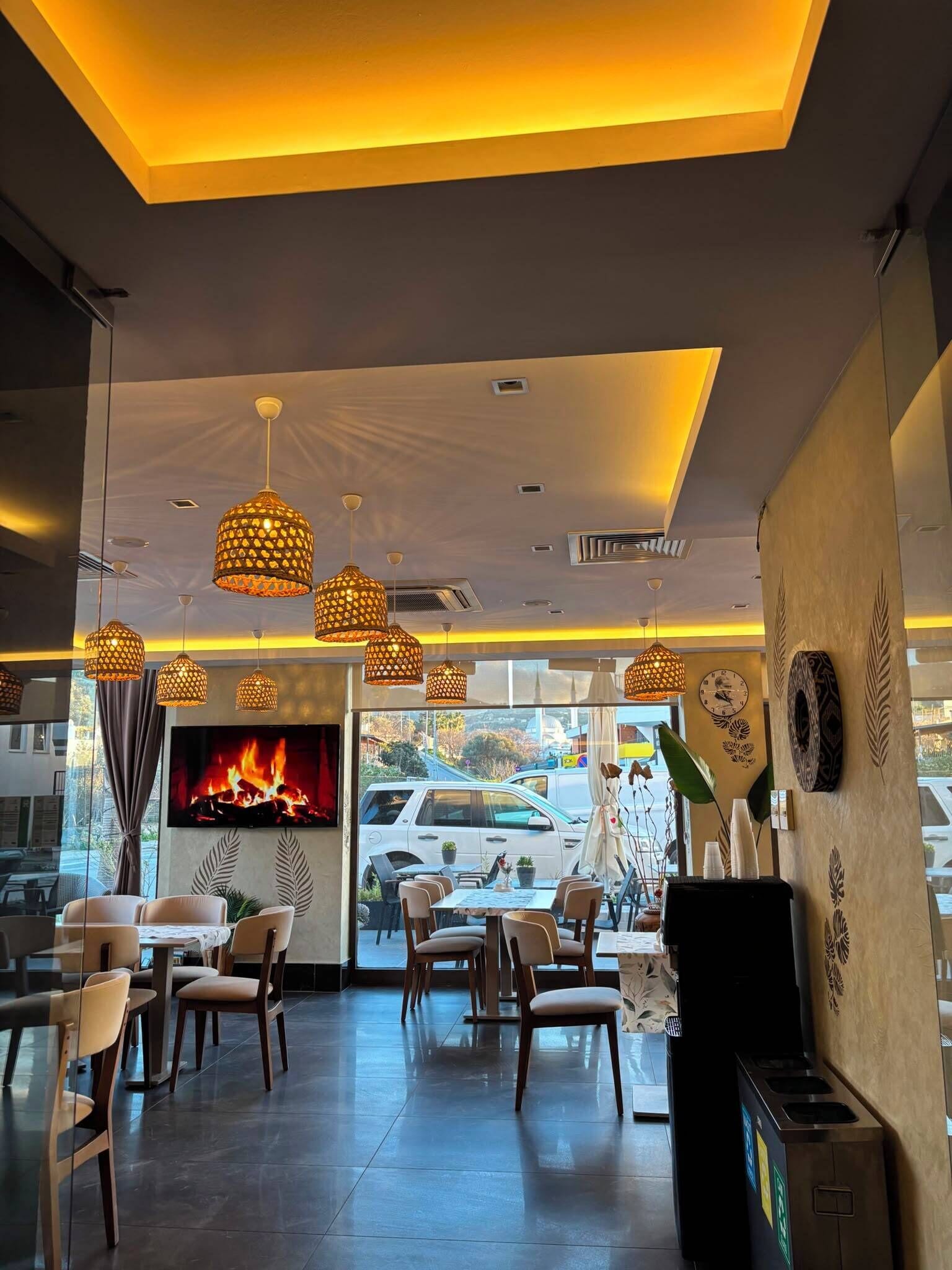 A restaurant interior with a fireplace, multiple hanging pendant lights, and a view of the outside.