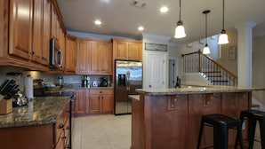 A kitchen with wooden cabinets, a stainless steel refrigerator, granite countertops, and a bar area with stools. - 🦩Book Me Baby! Destin Delight in The Villages of Crystal Lakes🦩 (Destin)