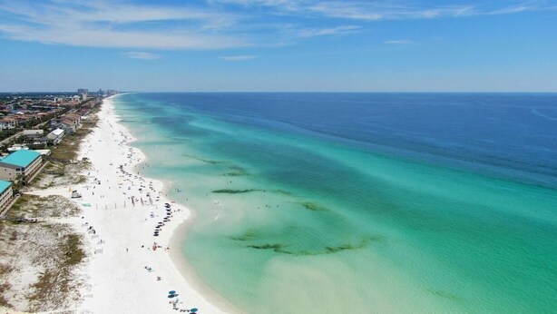 An aerial view of a beach with clear turquoise waters, a sandy shore, and buildings along the coastline. - 🦩Book Me Baby! Destin Delight in The Villages of Crystal Lakes🦩 (Destin)