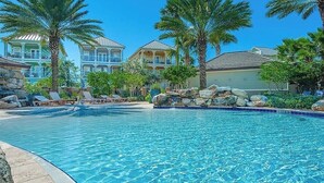 A swimming pool with lounge chairs and palm trees, surrounded by buildings with balconies. - 🦩Book Me Baby! Destin Delight in The Villages of Crystal Lakes🦩 (Destin)