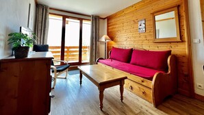 A cozy room with a wooden wall, a red sofa, a wooden table, a chair, and a potted plant.