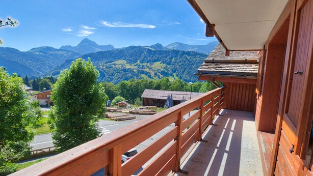 A balcony with a wooden railing overlooking a mountainous landscape.