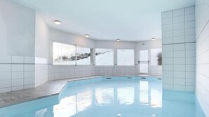 An indoor swimming pool with tiled walls and windows.