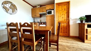 A wooden dining table with four chairs, a wooden cabinet, a microwave, and a television on a wooden stand.