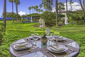 A round table set for four with a view of a landscaped garden and a body of water in the background.