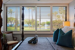 Ein Schlafzimmer mit Bett, einem Sessel, einem Fenster mit Jalousien und Blick auf einen Golfplatz.