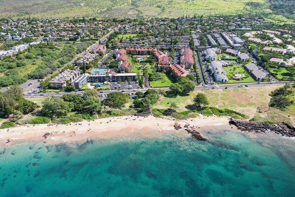 An aerial view of a coastal residential area with a beachfront, houses, and a large building complex.