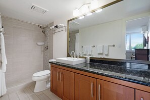 Ein modernes Badezimmer mit einer weißen Toilette, einem Waschbecken mit schwarzer Arbeitsplatte, Holzschränken und einem großen Spiegel.
