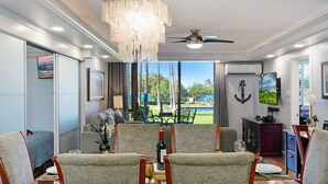 Un comedor con vista a una piscina y zonas verdes, un ventilador de techo y un televisor.