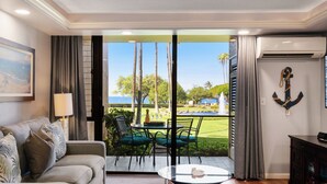 Una sala de estar con un sofá, una mesa y sillas. Se ve un jardín y palmeras desde el exterior.