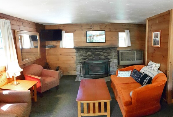 A cozy cabin interior with a stone fireplace, wooden walls, a sofa, a chair, and a small table.