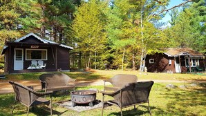 Eine rustikale Holzhütte mit Veranda und Sitzgelegenheit im Freien, umgeben von Bäumen.
