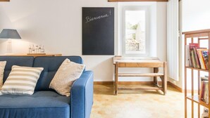Un soggiorno accogliente con un divano blu, un tavolino in legno, una lavagna con la scritta 'Bienvenue' e una libreria piena di libri.
