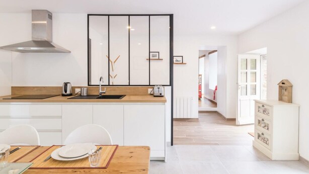 Una cucina moderna con mobili bianchi, un piano di lavoro in legno e una cappa aspirante in acciaio inossidabile.