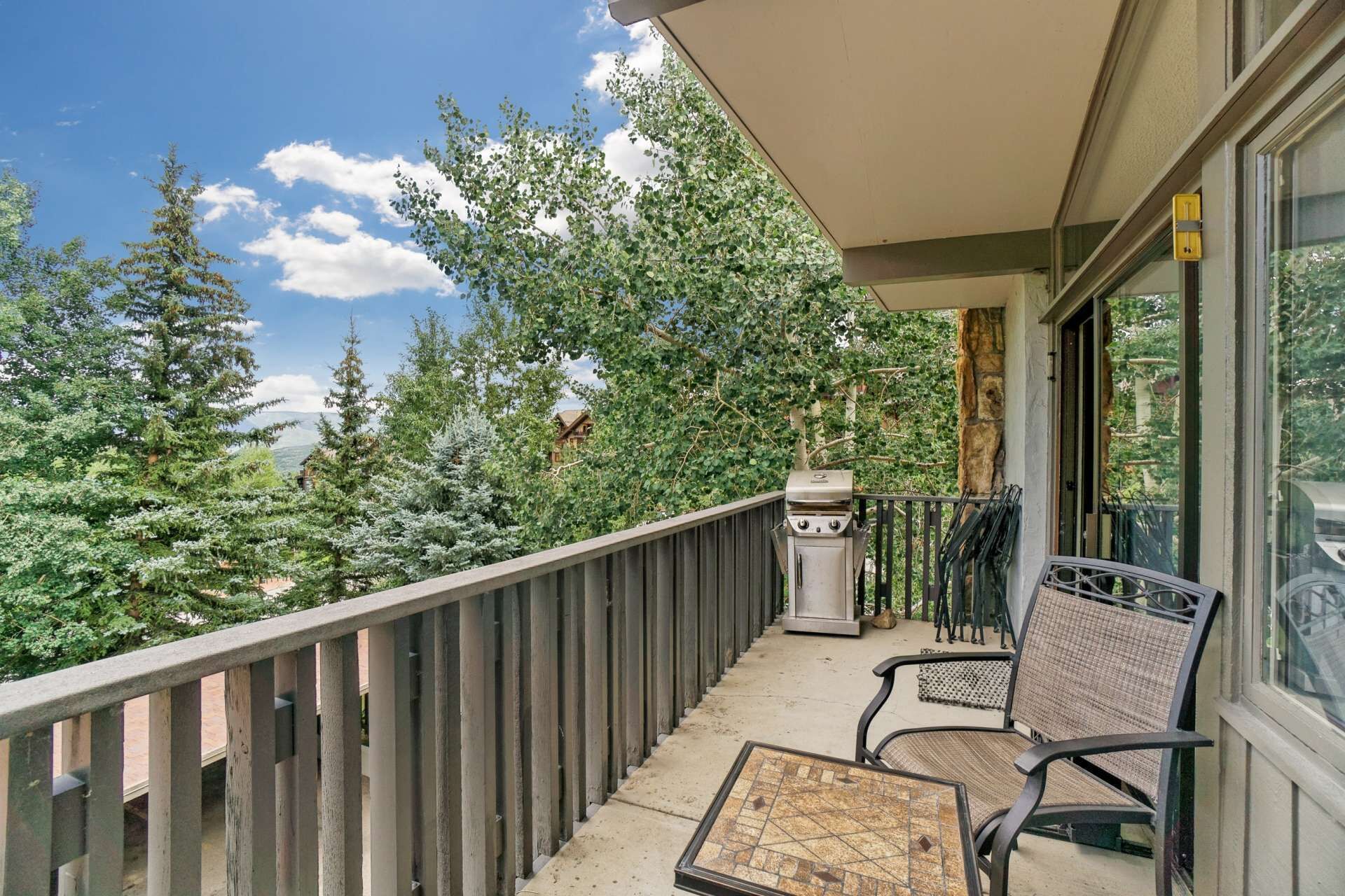 A balcony with a view of trees and a grill.