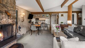 A cozy living room with a fireplace, a dining area, and a kitchen in the background. - Charming Condo Next To Base Village In Snowmass! Pool, HT, Balcony With Grill, Parking, W&D (Snowmass Village)