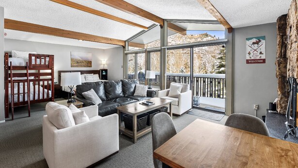A modern living room with a wooden ceiling, a sofa set, a coffee table, and a view of the outdoors. - Charming Condo Next To Base Village In Snowmass! Pool, HT, Balcony With Grill, Parking, W&D (Snowmass Village)