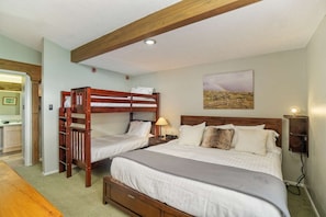 Um quarto com duas beliches, uma cama de solteiro, uma mesa de cabeceira com abajur e um quadro na parede.