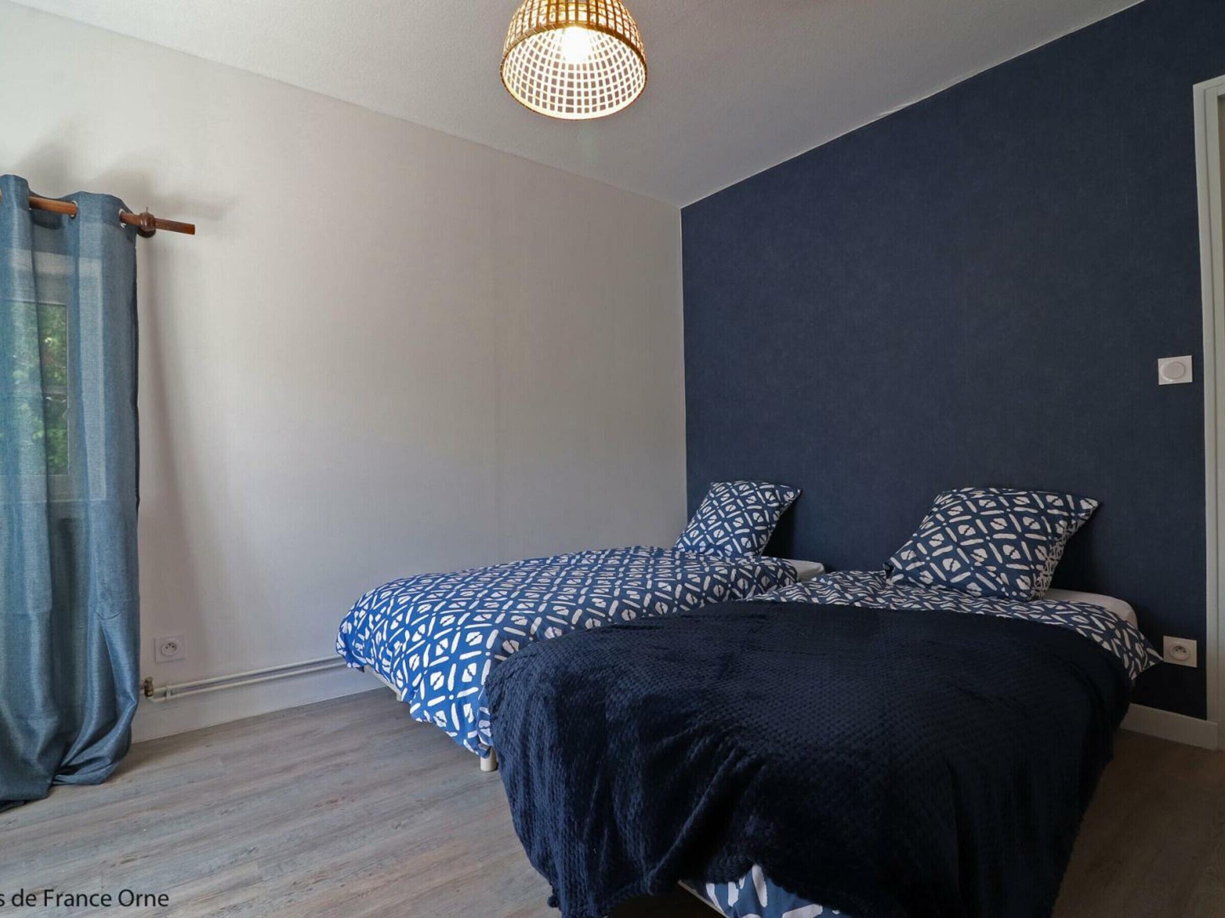 Un dormitorio con cama, mesita de noche, lámpara colgante y ventana con cortinas.