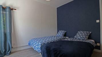 Un dormitorio con cama, mesita de noche, lámpara colgante y ventana con cortinas.