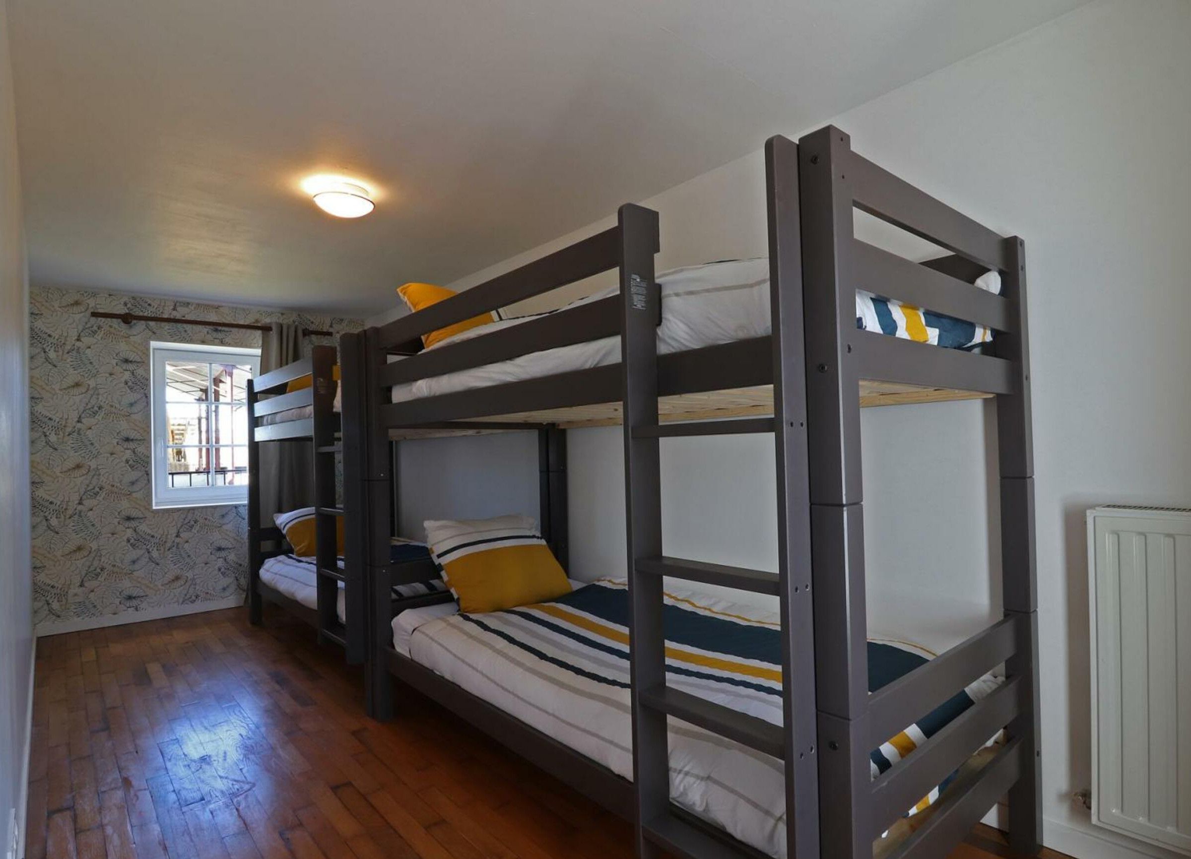 Een slaapkamer met stapelbedden van hout, een raam en een radiator.