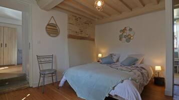 Een slaapkamer met een houten vloer, een bed met een lichtblauwe spreidekking, twee bedlampen, een stoel en een hangende lamp.