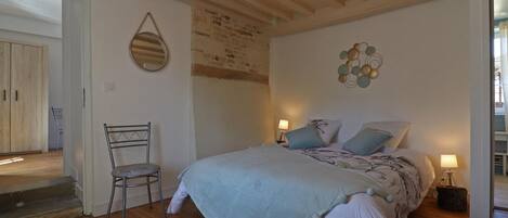 Un dormitorio con piso de madera, una cama con colcha azul claro, dos lámparas de noche, una silla y un candelabro.