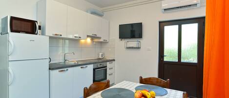 A compact kitchen with white cabinets, a microwave, a sink, and a dining table with placemats and a fruit bowl.