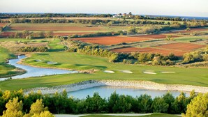 Ein Golfplatz mit Teich, Sandbunkern und Blick auf die umliegende Landschaft.