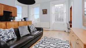 A modern living room with a black leather sofa, wooden cabinets, and a large window.