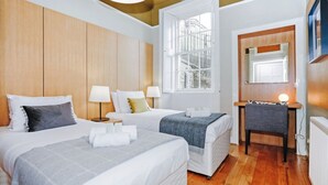 A hotel room with two beds, a desk, a chair, and a large window.