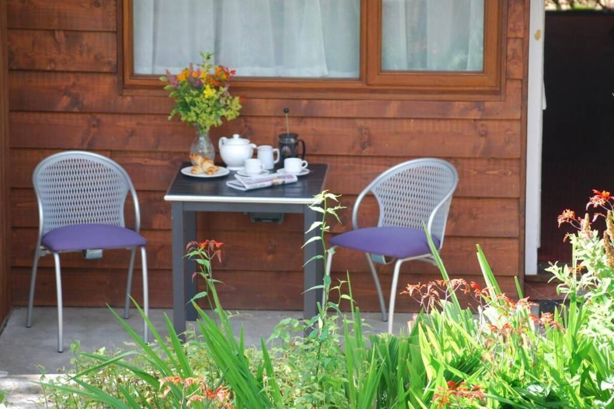 A wooden cabin with a table and two chairs, a vase with flowers, and a window with curtains.