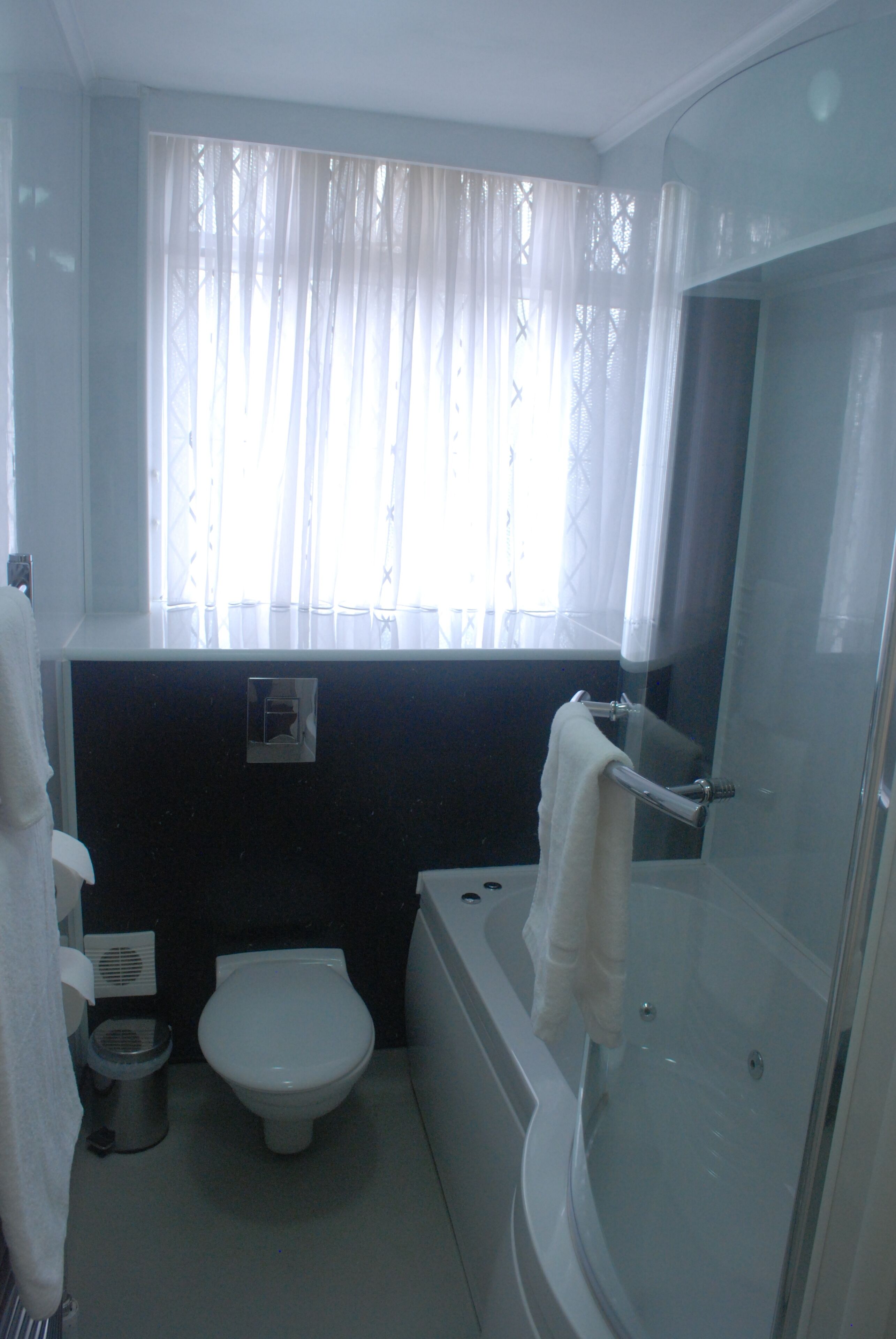 Une salle de bain équipée de toilettes, d’une baignoire et d’une fenêtre ornée de rideaux légers.