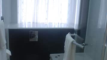 Un baño con inodoro, bañera y ventana con cortinas ligeras.
