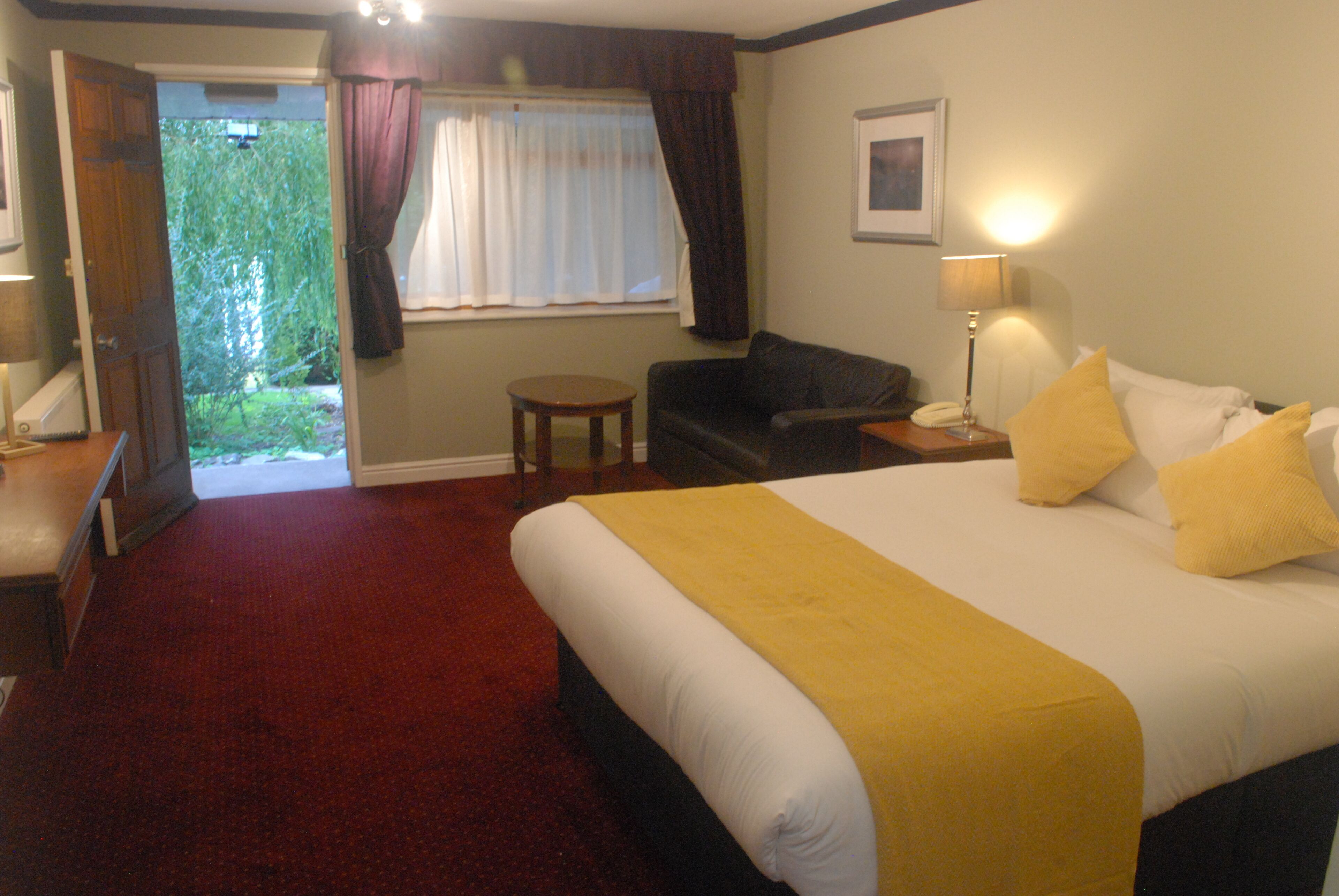 A hotel room with a large bed, a small round table, a sofa, and a window with curtains.
