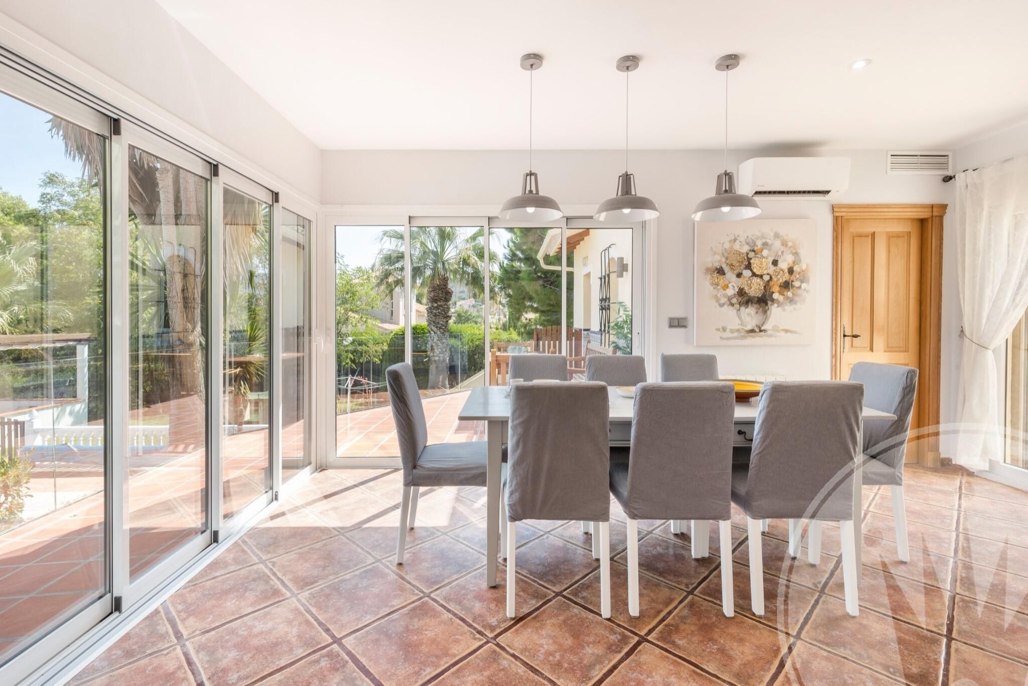A dining area with a table and chairs, large windows, and an air conditioning unit.