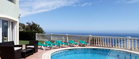 A pool with lounge chairs and a view of the ocean.
