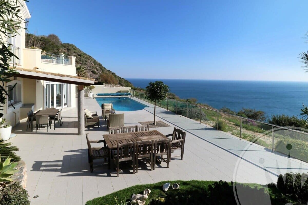 Eine Terrasse mit Pool, Gartenmöbeln und Blick auf das Meer.