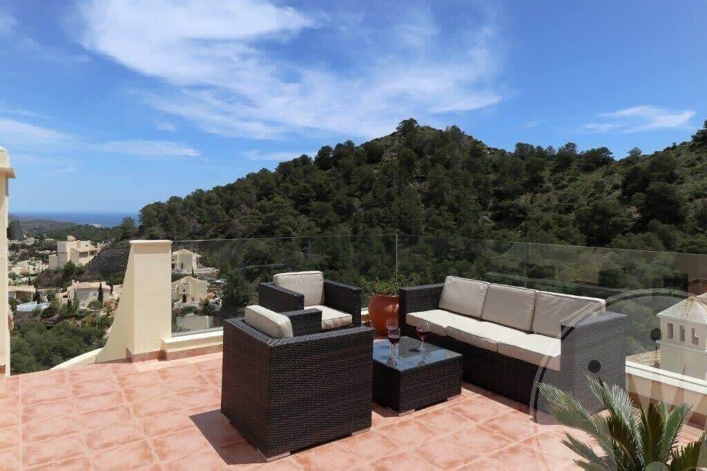 Une terrasse sur le toit, aménagée avec du mobilier d’extérieur, dotée d’une balustrade en verre et offrant une vue sur la ville et les collines.