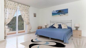 Une chambre à coucher avec un lit, une fenêtre avec des rideaux, un tableau au mur et une table de chevet avec une lampe.