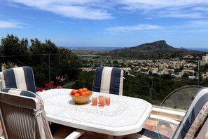 Une table avec des chaises et un saladier de fruits, donnant sur une ville et des collines.